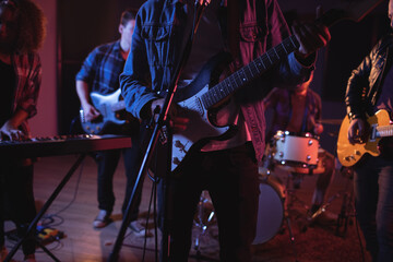 Midsection of diverse music band with guitarists and keyboard player during concert in music venue