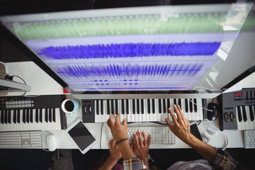 Midsection of two men using keyboard, computer with graphic music equalizer