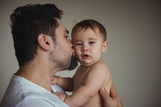 Caucasian father holding and kissing toddler looking at camera