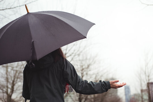 Rear view of caucasian woman with umbrella holding hand out checking rainfall