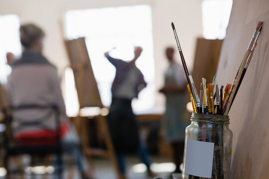 People working at a painting class in an art studio, a jar of paintbrushes in the foreground