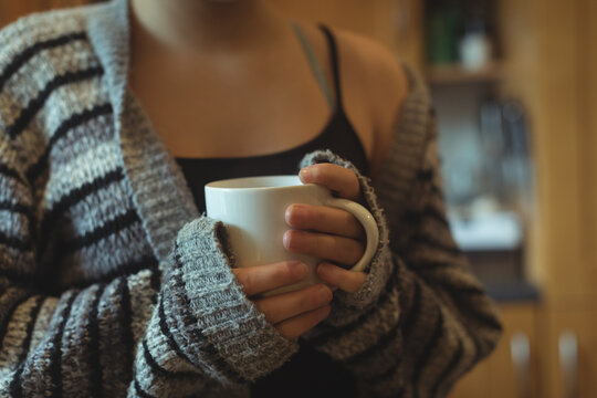 Midsection of caucasian woman in grey striped cardigan holding white cup at home