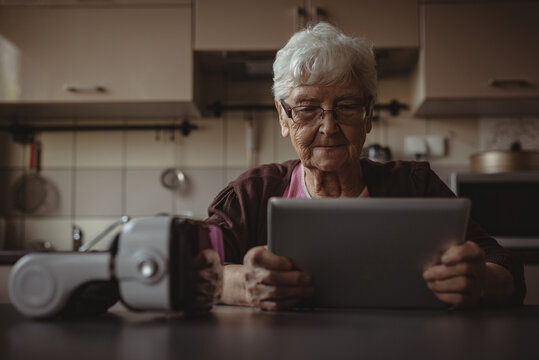 Portrait of senior woman sitting in kitchen, using tablet