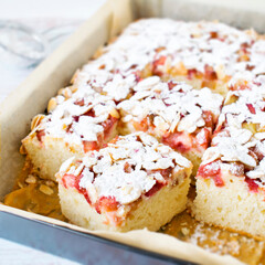 Homemade cake - yoghurt cake with rhubarb, sprinkled with almond flakes and powdered sugar.