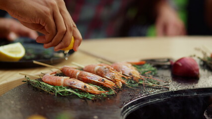 Unknown person squeezing lemon on shrimp outdoors. Prawns browning with herbs