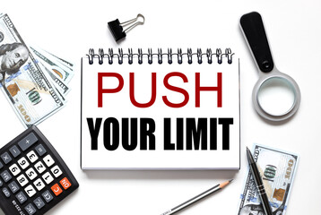 PUSH YOUR LIMIT. notebook on white workspace. near the notepad dollar bills and a calculator