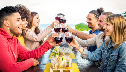 Multiracial group of friends enjoying wine in a bar restaurant at sunset in summer making a toast. Young people holding wine toasting and cheering. Friendship, youth, joy and togetherness concept