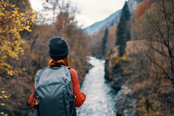woman hiker with a backpack on her back near a mountain river in nature, back view