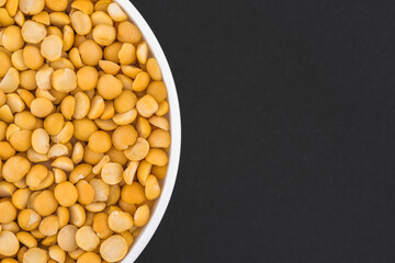 White glass bowl of yellow peas. Isolated on a dark grey background. Top view