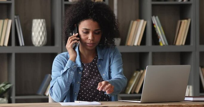 African female sit at workplace desk reading written information on paper comparing sharing data stats statement to colleague by phonecall, solve business on phone, talking to client remotely concept