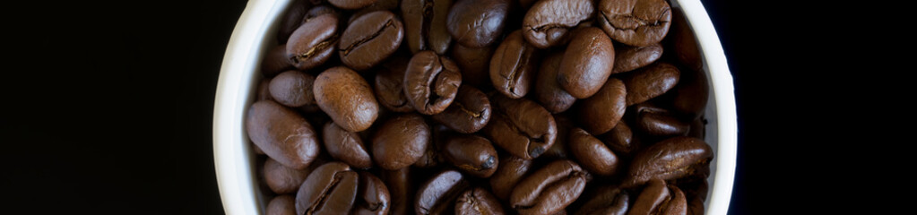 White mug filled with coffee beans on a dark background. Fragment. View from above. Web banner
