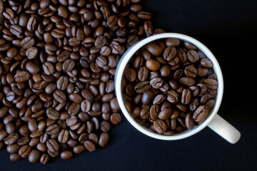 White coffee mug and lots of roasted coffee beans. Dark background. View from above