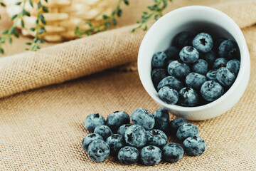 Tilted white bowl filled with fresh blueberries on a rustic background.
