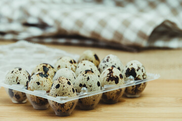 Plastic box of 12 quail eggs on wooden base.