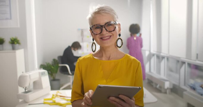 Mature businesswoman using tablet computer in studio of startup fashion business