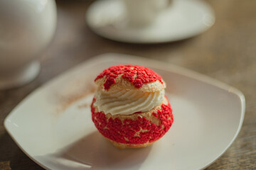 Choux pastry ball with vanilla cream, with red decor on white plate. Traditional French dessert. Close up with shallow dof.