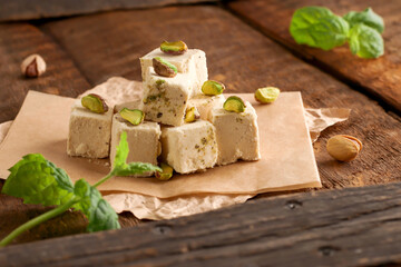 Walnut halva with pistachios on parchment paper on a wooden background. Traditional oriental dessert Chekme. Natural vegan product. Turkish, Arab and Jewish national sweets.