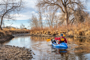 senior male  is paddling an inflatable packraft on a river in early spring spring - Poudre River in northern Colorado