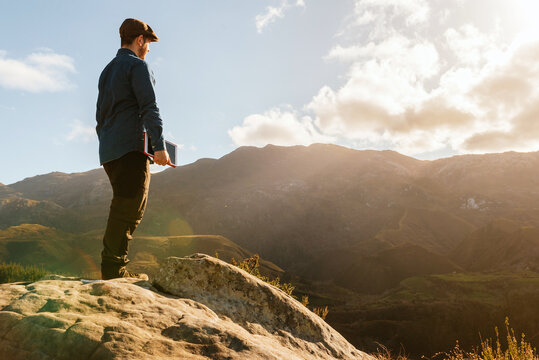 Side view of tranquil male explorer with tablet standing on rock and enjoying spectacular view of mountains on sunny day