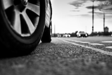 Sunset in the city, the approaching car on the highway. Close up view from the level of a parked car wheels