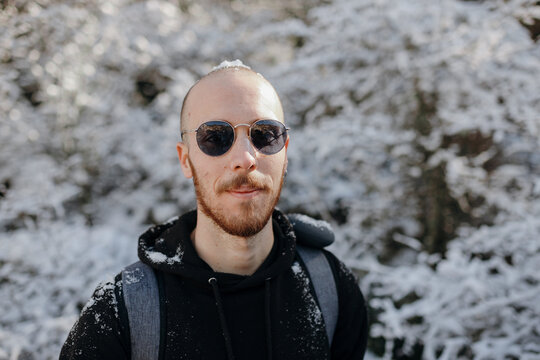 Bearded male backpacker looking at camera against snowy trees during journey on sunny day