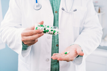 Crop anonymous male physician in uniform pouring medications from bottle on hand at work in hospital