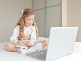 Happy little girl learning online with computer at home. Online school concept.