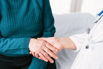 Crop anonymous doctor speaking with elderly woman while holding hands during examination in hospital