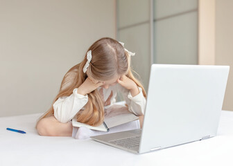 Sad little girl learning online with computer at home. Online school concept. Difficulties learning at school.