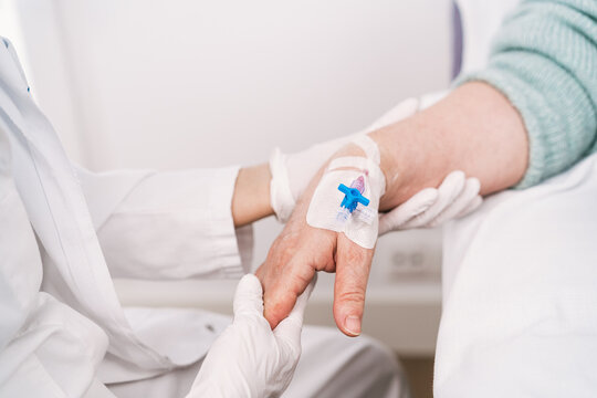 High angle of crop anonymous medic in disposable gloves putting intravenous catheter on arm of patient in hospital