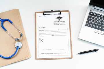 From above modern medical workspace with laptop, stethoscope and paper form on clipboard on desk in hospital
