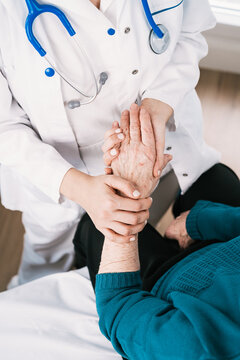 From above crop anonymous doctor speaking with elderly woman while holding hands during examination in hospital