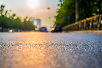 Sunset in the city, the empty road with parked cars. Close up view from the asphalt level
