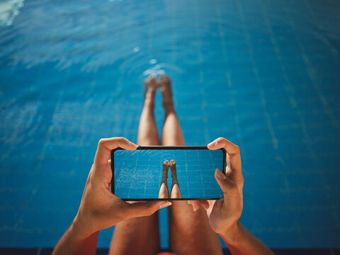 From above of crop anonymous barefoot female taking photo of legs on cellphone over swimming pool with pure water
