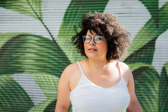 Content adult overweight female in eyewear curly hair against ornamental wall in daytime