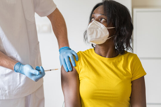 Cropped unrecognizable male medical specialist in protective latex gloves vaccinating female African American patient in clinic during coronavirus outbreak