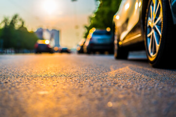 Sunset in the city, the cars traveling on the road. Close up view from the level of a parked car...