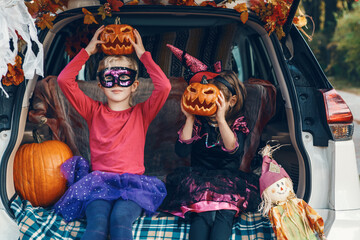 Trick or trunk. Children siblings sisters celebrating Halloween in trunk of car. Friends kids girls...