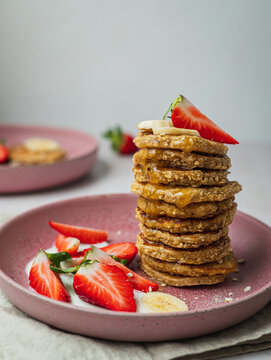 Plate with a row of banana pancakes and a few pieces of strawberries