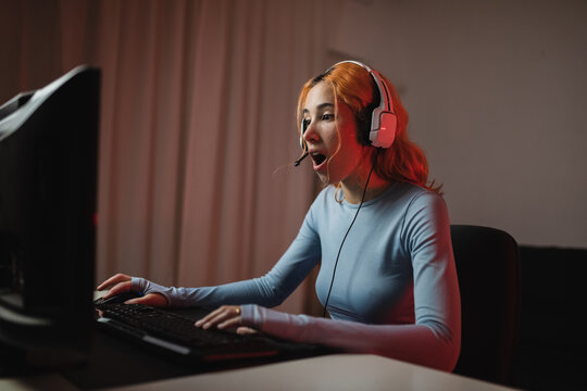 Side View Of Delighted Female Gamer In Headphones Playing Videogame While Sitting At Table At Home