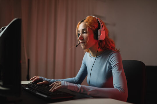 Side view of delighted female gamer in headphones playing videogame while sitting at table at home