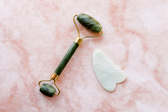 Top view of jade roller and guasha scraper arranged on marble table for concept of face massage
