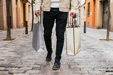 Cropped unrecognizable man with shopping bags strolling on urban walkway