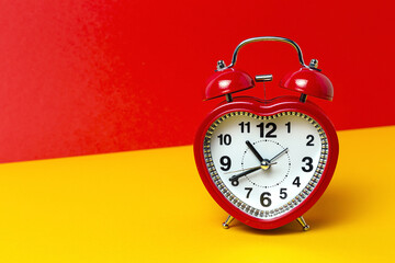 Red metal alarm clock in shape of heart placed on vibrant two colored background in studio