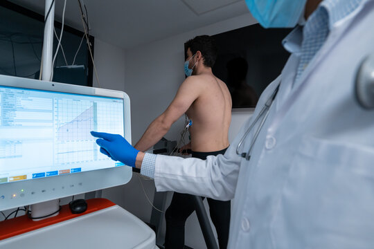 Crop medic analyzing data on digital monitor during cardiac stress test of male patient walking on treadmill