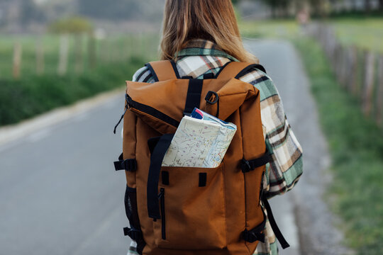 Back view of crop anonymous female hiker with route map in backpack on roadway in countryside