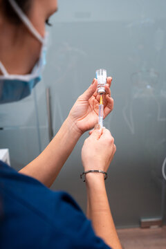 Side view of cropped unrecognizable female veterinarian in cloth face mask taking medicine with injector from bottle
