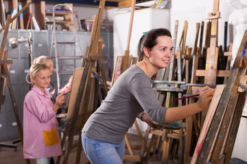 Positive woman teacher giving workshop session during painting class at art studio.
