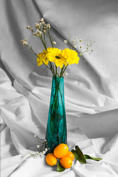 Bright blossoming chrysanthemums with pleasant aroma and sprigs in vase on crumpled white textile with fresh kumquats
