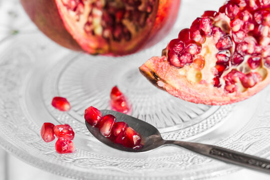 Bright tasty fresh pomegranate with ripe seeds and blooming flower sprig on transparent stand on crumpled fabric